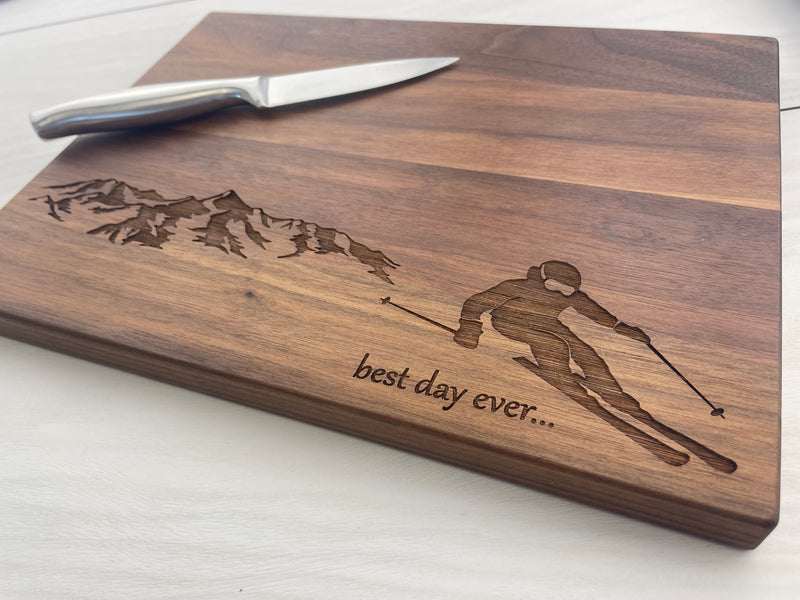 A personalized wooden cutting board with a laser engraved image of a skier and the phrase 'best day ever.
